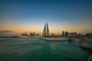 Modern buildings silhouetted at sunset over water.